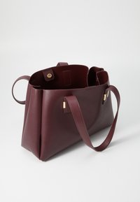 Sac tote en cuir bordeaux avec des côtés plats, deux poignées et une sangle d'épaule. Présente des accessoires en ton doré et un design à ouvert.