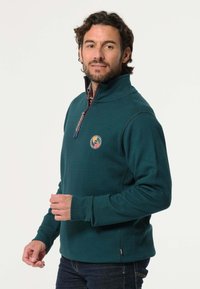 Donkerblauwe fleecetop met een half-rits kraag, met een ronde logo op de borst en een contrasterende patroonvoering. Zachte textuur.