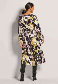 Langarmkleid mit einem mehrfarbigen abstrakten Muster in Schwarz, Gelb und Creme. Hergestellt aus glattem Stoff mit einem lockeren Schnitt.