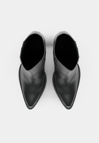 Bottes en cuir noir à la cheville avec un bout pointu et une texture lisse. Elles présentent un talon bas et des coutures discrètes sur les côtés.