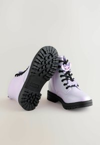 Lilac læder ankelstøvler med sort gummisål, der har en tekstureret sål, sorte snøre og dekorative elementer formet som tegneseriefigurer.