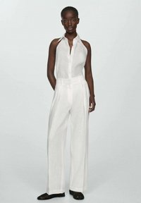 Top halter alb din in cu închidere cu nasturi, combinat cu pantaloni albi cu picioare largi. Material texturat, linii curate și croială îngrijită. Sandale negre.