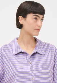 Camicia con colletto a righe viola e bianche, con bottoni, caratterizzata da un tessuto morbido e strutturato e una vestibilità rilassata. Decorata con un colletto curato.