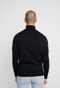 Schwarzer Rollkragenpullover, taillierte Passform, lange Ärmel, glatte Textur, gerippter Kragen und Saum, getragen mit hellblauen Jeans.