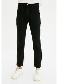 Vaqueros de mezclilla negros de cintura alta con bolsillos delanteros, una textura suave y un diseño de pierna ajustada, combinados con zapatillas blancas.