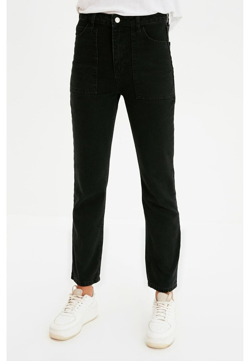 Vaqueros de mezclilla negros de cintura alta con bolsillos delanteros, una textura suave y un diseño de pierna ajustada, combinados con zapatillas blancas.