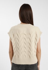 Maglione lavorato a maglia beige con motivo a treccia, maniche corte e orlo a coste. Texture morbida con scollatura aderente.