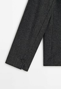 Manche de manteau en laine gris foncé avec un seul bouton noir près du poignet, montrant une couture propre et une couture droite sur fond blanc.