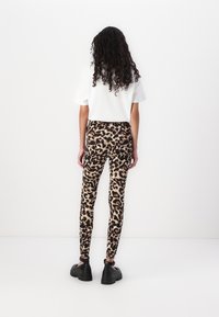 Leggingi z vzorcem leoparda s prilegnjenim dizajnom, ki imajo svetlo bež podlago in temno rjave pike, v kombinaciji z belim kratkoročnim zgornjim delom in masivnimi črnimi čevlji.