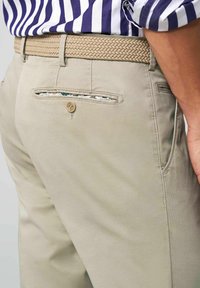 Beige cotton trousers feature a braided tan belt, back pocket with a button, and subtle textured fabric for a polished look.