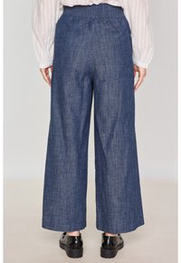 Pantaloni a gamba larga in denim blu scuro con fascia elastica in vita. Il tessuto ha una texture liscia, con una vestibilità comoda che si drappeggia in modo uniforme.