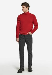 Röd stickad polotröja med ribbade manschetter och nederkant, kombinerad med mörkgrå rakbenade byxor och svarta snörskor. Enslig bakgrund.