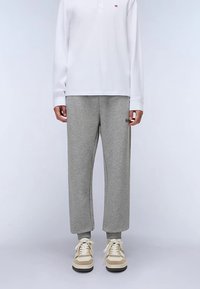 Graue Sweatpants mit lockerem Schnitt und weicher Textur. Kombiniert mit einem weißen Langarm-Poloshirt und beigen Sneakern mit weißen Akzenten.