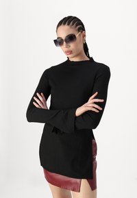 Black long-sleeve top with ruffled neckline, paired with a burgundy leather mini skirt. Model wears oversized sunglasses.