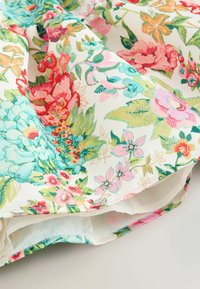 Tkanina s cvetličnim vzorcem, ki prikazuje velike rožnate, rdeče, modre cvetove in zelene liste na belem ozadju, nežno prepognjena.