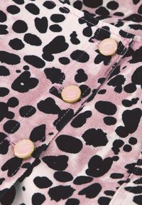 Roze stof met zwart luipaardprint en goudkleurige hardware knopen. Zichtbare stikdetails vergroten de textuur. Close-up view.