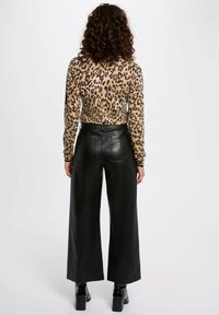 Top de manga larga con estampado de leopardo combinado con pantalones anchos de piel negra de cintura alta, que presentan una textura suave y un ajuste a medida.