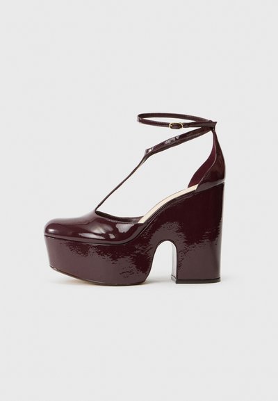 Chaussures à plateforme en cuir verni bordeaux avec un talon épais et courbé et une bride de cheville, présentant un design découpé sur le dessus.