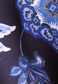 Gros plan d'un tissu avec des motifs floraux bleus complexes et des feuilles sur un fond sombre, avec un ombrage et des contours détaillés.