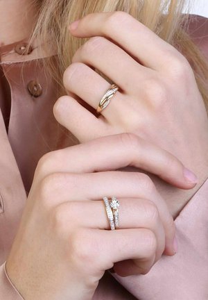 Gouden en zilveren ringen, de ene met een gedraaide ontwerp en kleine diamanten, de andere een klassieke band met een centrale steen, gedragen op slanke vingers.