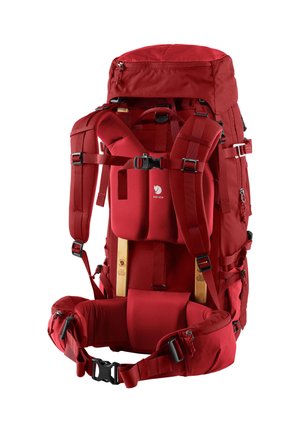 Sac à dos en tissu rouge avec des bretelles rembourrées et des sangles de taille, plusieurs compartiments et une poche zippée en haut. Inclut un cadre en bois pour le soutien.