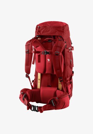 Sac à dos en tissu rouge avec des bretelles rembourrées et des sangles de taille, plusieurs compartiments et une poche zippée en haut. Inclut un cadre en bois pour le soutien.