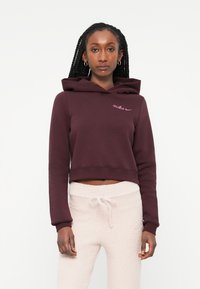 Vınna kratka kapuca v maroon barvi z vrvico, vsebuje roza Nike logotip na prsih. Ujemajoče se teksturirane smetane barve trenirke.
