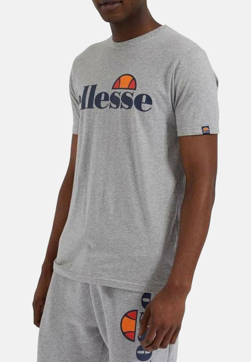 Homme portant un t-shirt gris Ellesse et un short assorti, avec un logo Ellesse audacieux imprimé sur le t-shirt et le short.