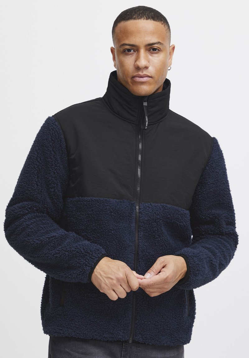 Fleece jacket featuring a navy and black color block design, zip closure, high collar, and textured fabric with side pockets.