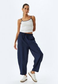 Marineblaue weite Hose mit elastischem Bund und Kordelzug. Kombiniert mit einem weißen Spaghettiträger-Top und lässigen weißen Sneakers.