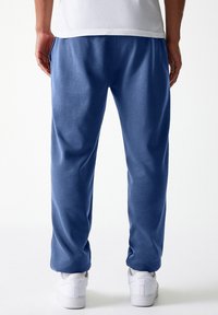 Pantalons de survêtement en coton bleu avec une taille élastique, des poches latérales et une coupe décontractée, associés à des baskets blanches.