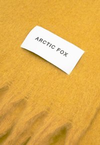 Gelbes, flauschiges Material mit einem weißen Etikett, auf dem "ARCTIC FOX" in fetter schwarzer Schrift steht. Das Material wirkt weich und strukturiert.
