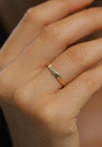 Close-up of a hand with a smooth, plain gold band worn on the ring finger against a blurred background.