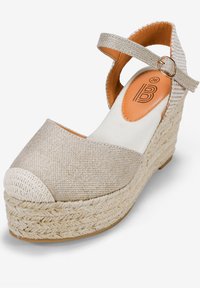 Sandale compensée en espadrille beige avec une tige texturée, bout rond, bride de cheville, semelle en jute tissé et détails intérieurs marron.