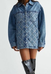 Denim jacket with a light blue hue, featuring diamond-patterned rhinestone embellishments, button closure, and oversized fit.