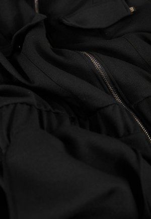 Black garment with visible zipper and gathered fabric texture. Features flat pockets and a soft, smooth material.