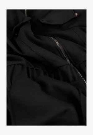 Zwarte kledingstukken met zichtbare rits en gathered stoftextuur. Bevat platte zakken en een zachte, gladde stof.