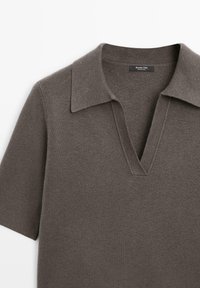 Polo in maglia marrone a maniche corte con colletto a V aperto, texture morbida e stile casual, distesa su uno sfondo bianco.