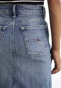 Gonna di jeans di un blu chiaro con un design aderente, cuciture visibili e due tasche posteriori. Presenta un piccolo dettaglio del logo sulla tasca.