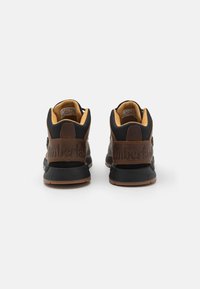Zapatillas altas negras y marrones con un respaldo de cuero texturizado, suela de goma y marca en relieve. El interior cuenta con un forro beige.
