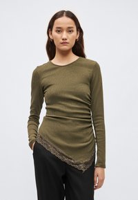 Ilgas rankovėmis, alyvuogių žalumos viršus su ribuota tekstūra ir nėriniuota apdaila ties apačia. Dizainas turi suspausto audinio detales šone.