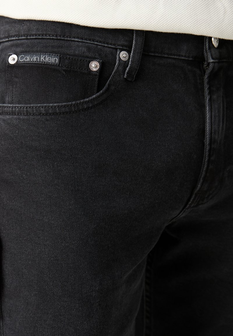 Czarne dżinsy w kolorze denimu o matowym wykończeniu, z przednią kieszenią, srebrnymi elementami metalowymi oraz metką Calvin Klein na tylnej części pasa.