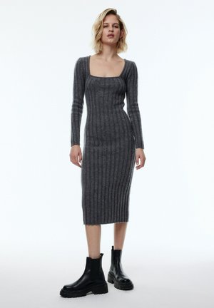 Graues, geripptes Midi-Kleid mit langen Ärmeln und viereckigem Ausschnitt, kombiniert mit schwarzen, klobigen Stiefeletten.