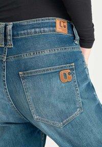 Jeans de mezclilla azul con un corte relajado, que cuentan con un logotipo de parche de cuero marrón en la cintura y un bolsillo trasero con un acento de logotipo.