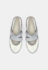 Ανοιχτό γκρι και κρεμ παπούτσια χωρίς κορδόνια με στρογγυλεμένη μύτη, που διαθέτουν δύο ρυθμιζόμενα λουριά και υφή από καουτσούκ στην σόλα. Κατασκευασμένα από λείο δέρμα και σουέτ υλικά.