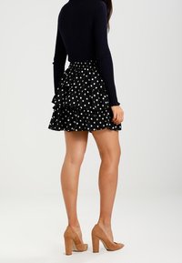 Mustikka lipunnauha, jossa on kerrokselliset rypyt, yhdistettynä istuvaan laivastonsiniseen yläosaan. Korkokengät ovat beigejä ja lohkomuotoisia. Liukuvat kankaat, rento tyyli.