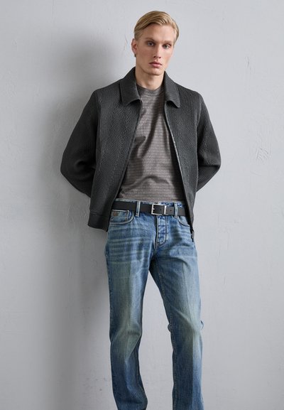 Gray textured jacket with a collar, layered over a gray patterned shirt. Light blue jeans with subtle fading and a black belt.