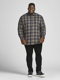 Plaid button-up shirt in navy, green, and yellow, paired with black slim-fit jeans and gray shoes. Casual design with long sleeves.