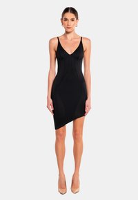 Schwarzes Bodycon-Kleid mit tiefem V-Ausschnitt, dünnen Trägern, strukturierten Nähten und asymmetrischem Saum. Getragen mit nudefarbenen High Heels.