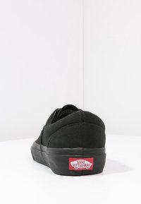 Černé plátěné tenisky s nízkým profilem, polstrovaným golfem a gumovou podrážkou. Na patě je umístěno červené logo "VANS OFF THE WALL".